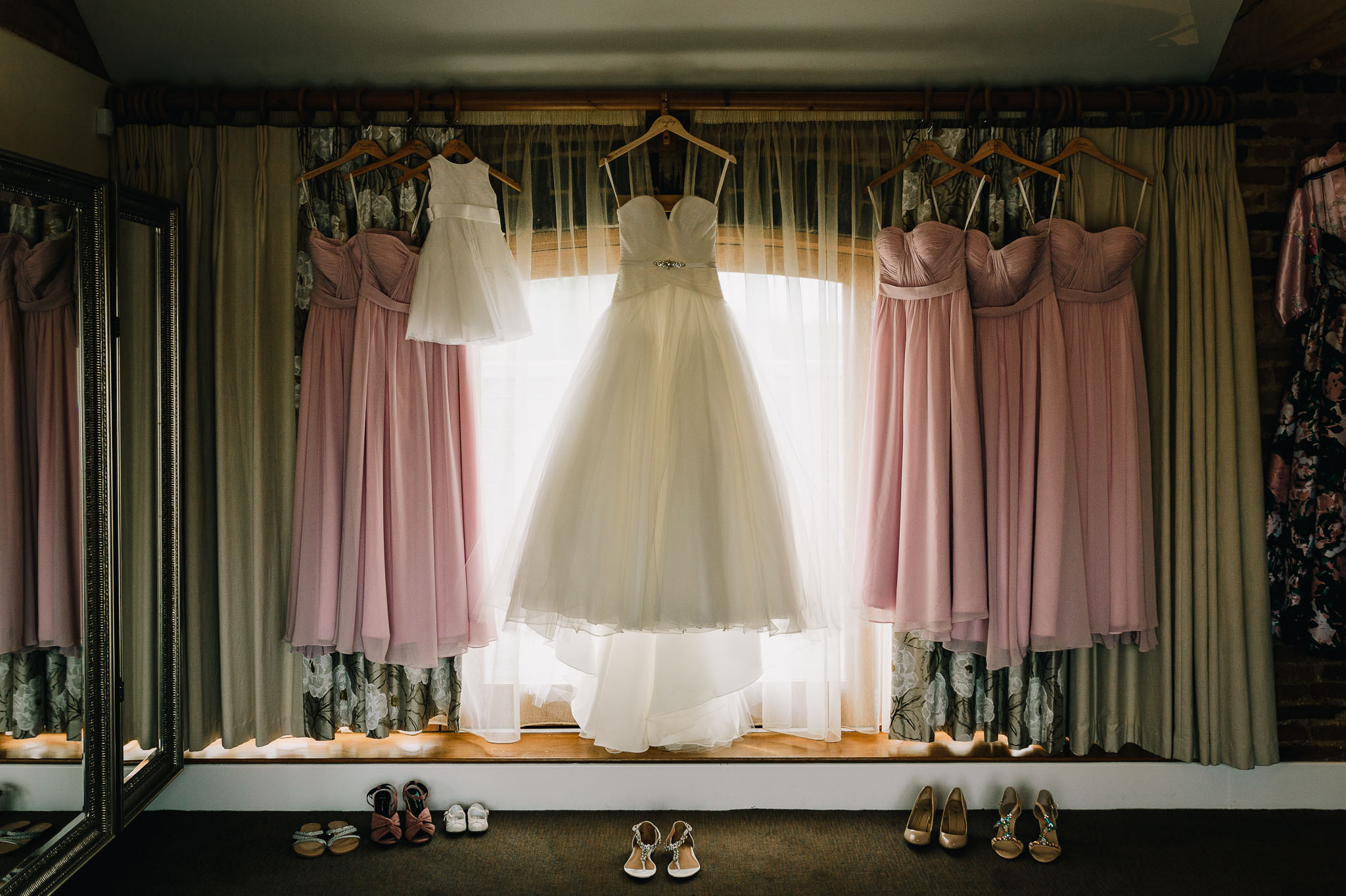 WEDDING DRESS AND BRIDESMAIDS DRESSES HANGING IN WINDOW WITH SHOES