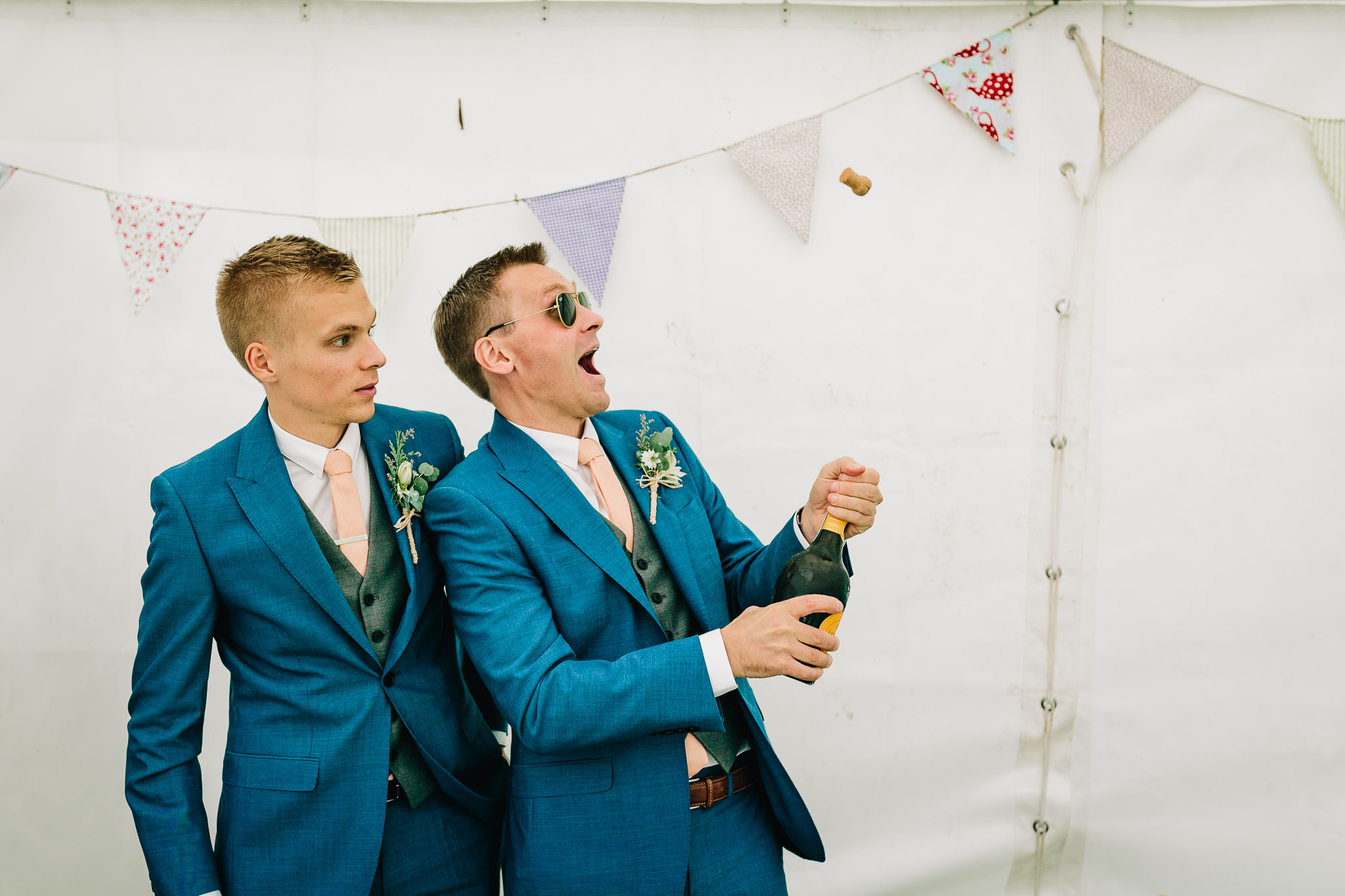 NATURAL PHOTO OF GROOMSMEN POPPONG CORK FROM CHAMPAGNE BOTTLE AT WEDDING RECEPTION