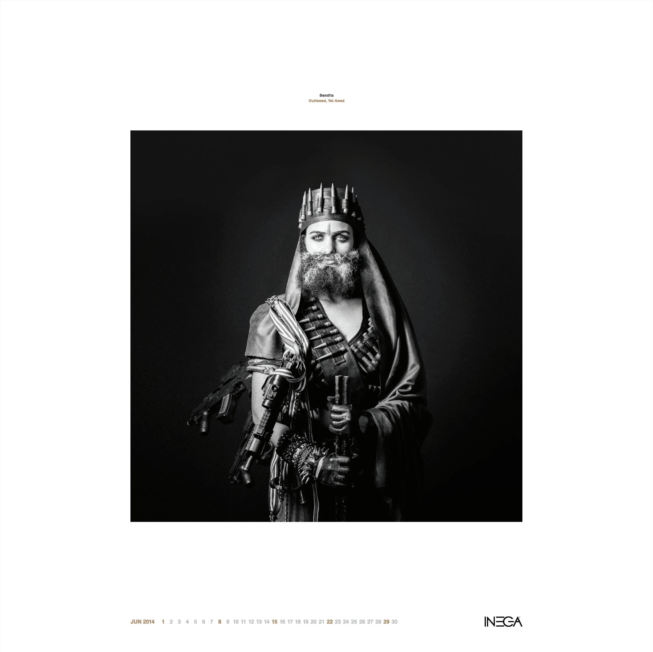 Black and white photo of a person with a crown, extensive beard, and costume holding a sword, dressed in a warrior or royal costume, against a dark background.
