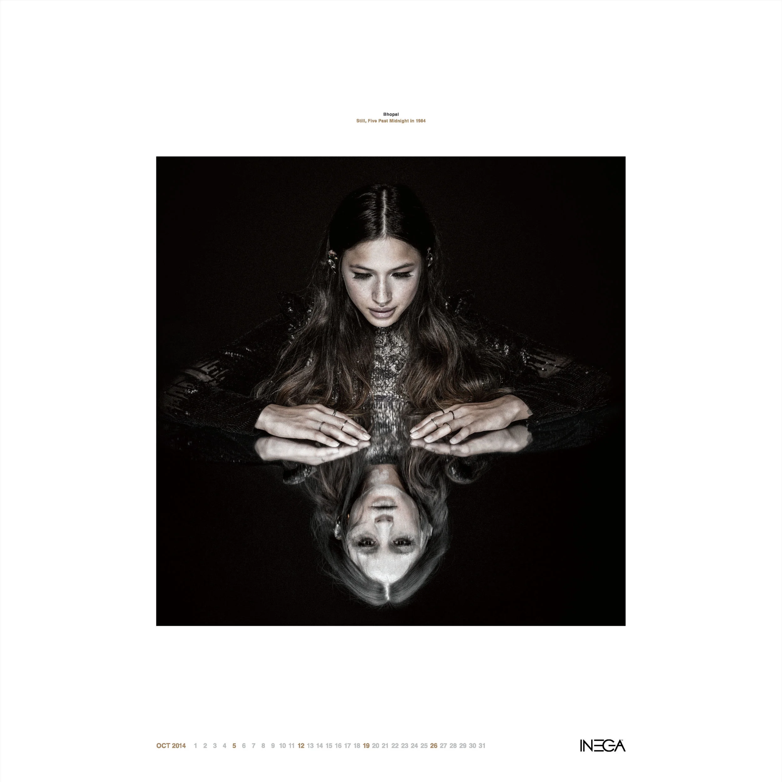 A woman with long brown hair leaning over a reflective black surface, her reflection visible beneath her, set against a dark background