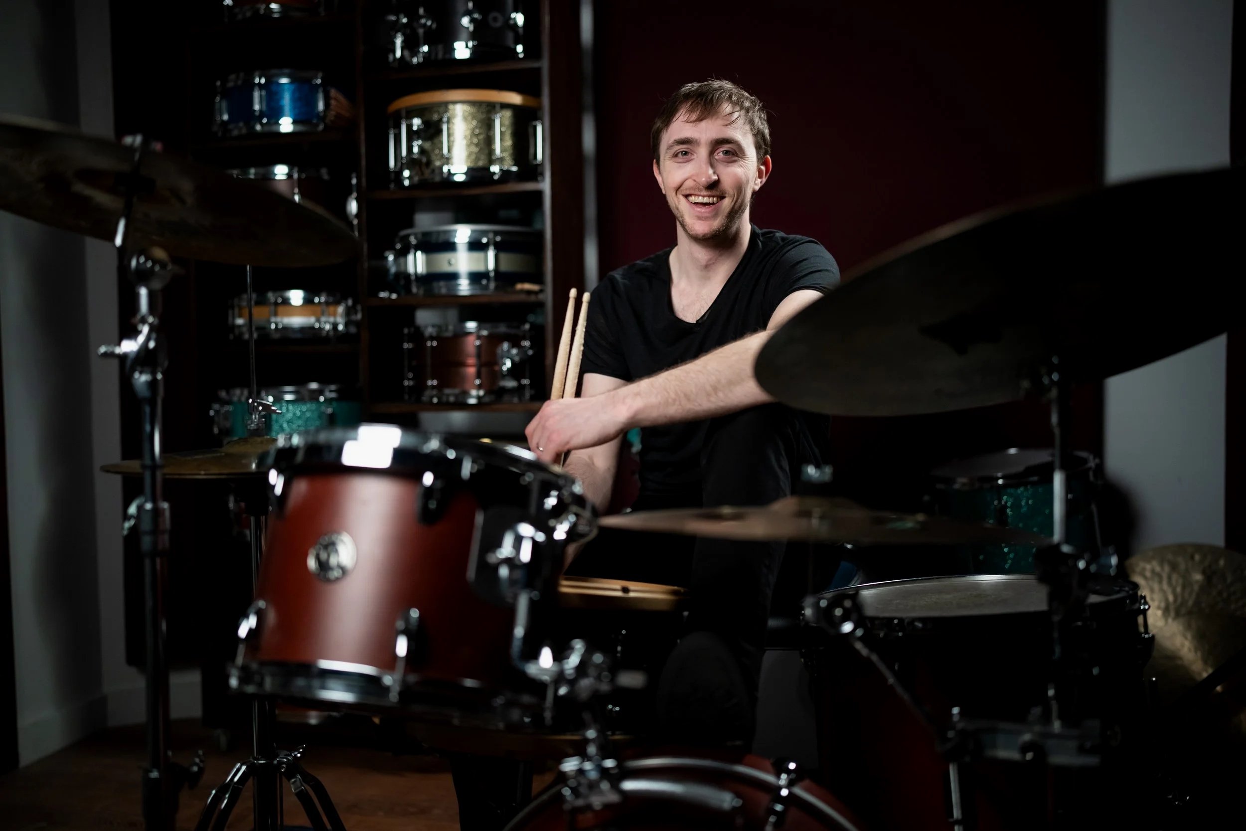 Matt sitting at a drum set with additional drums in the backgound
