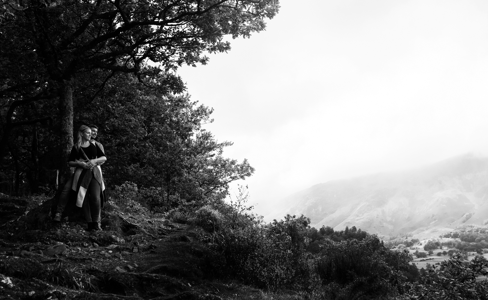 Wide image in black and white of Laura and Johnny looking over the lake with the Borrowdale valley in the background