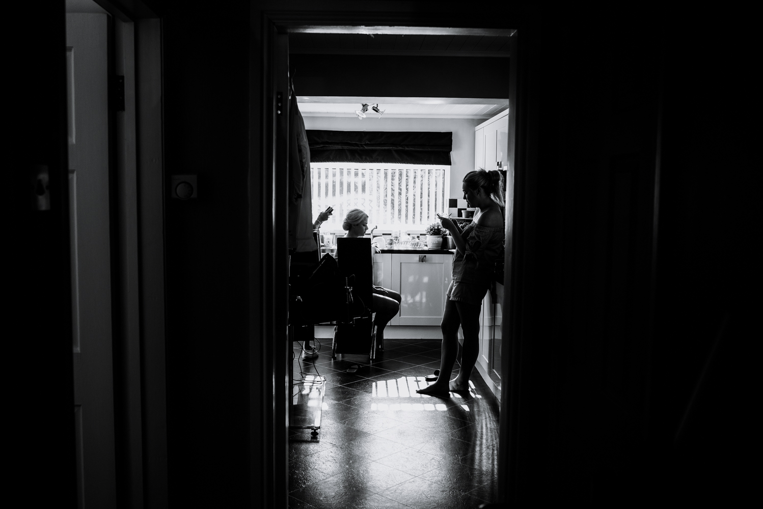 Black and white shot from the bottom of the hallway looking into the kitchen during bridal preparations