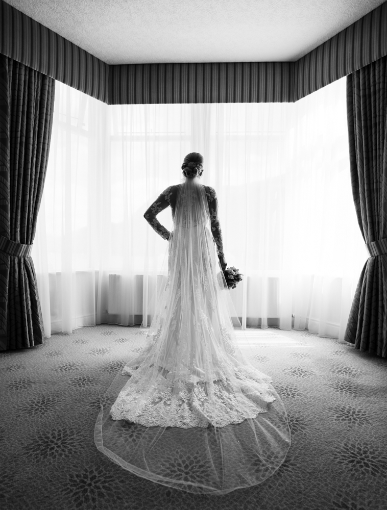 The bride standing in the bay window showing the back of her wedding dress