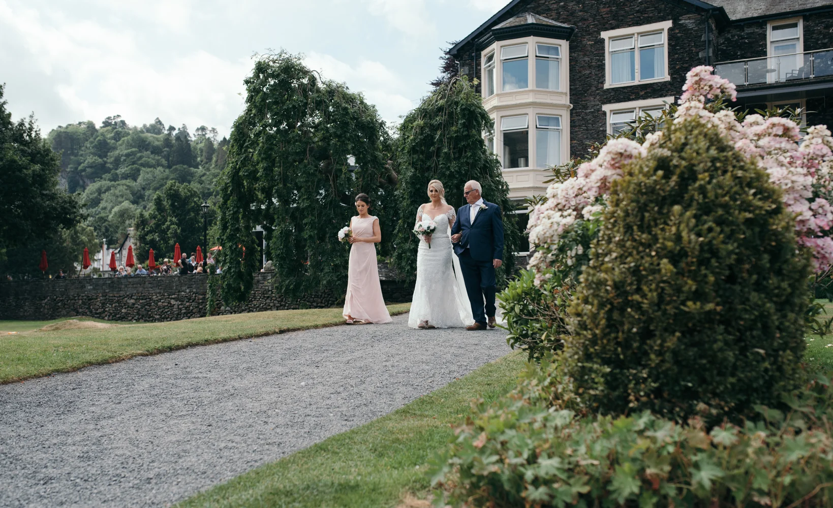 The bride with her father and bridesmaid walking down to the edge of the lake to get married