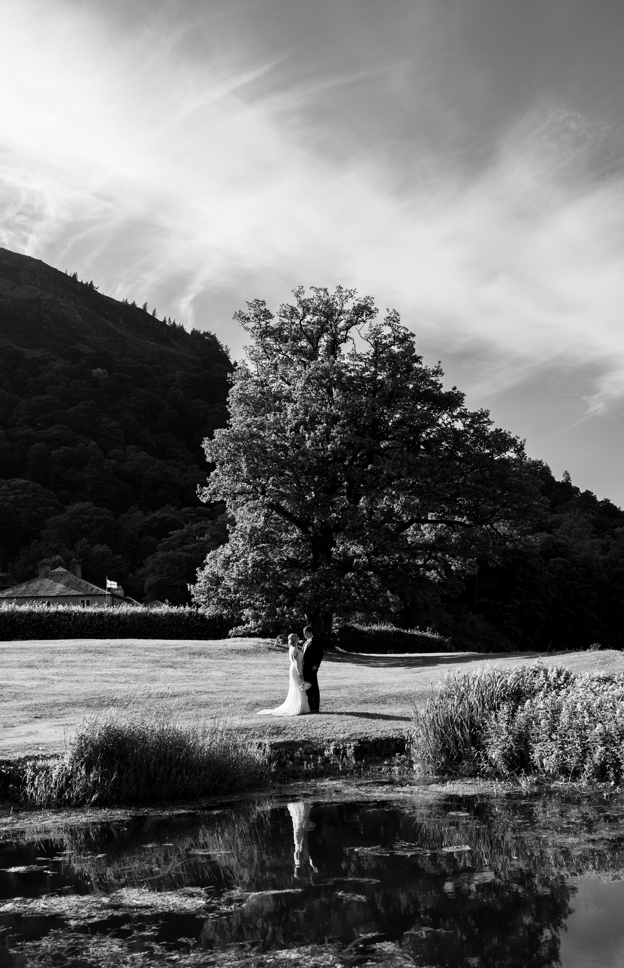 Black and white image of the bride and groom standing near the reflection pool