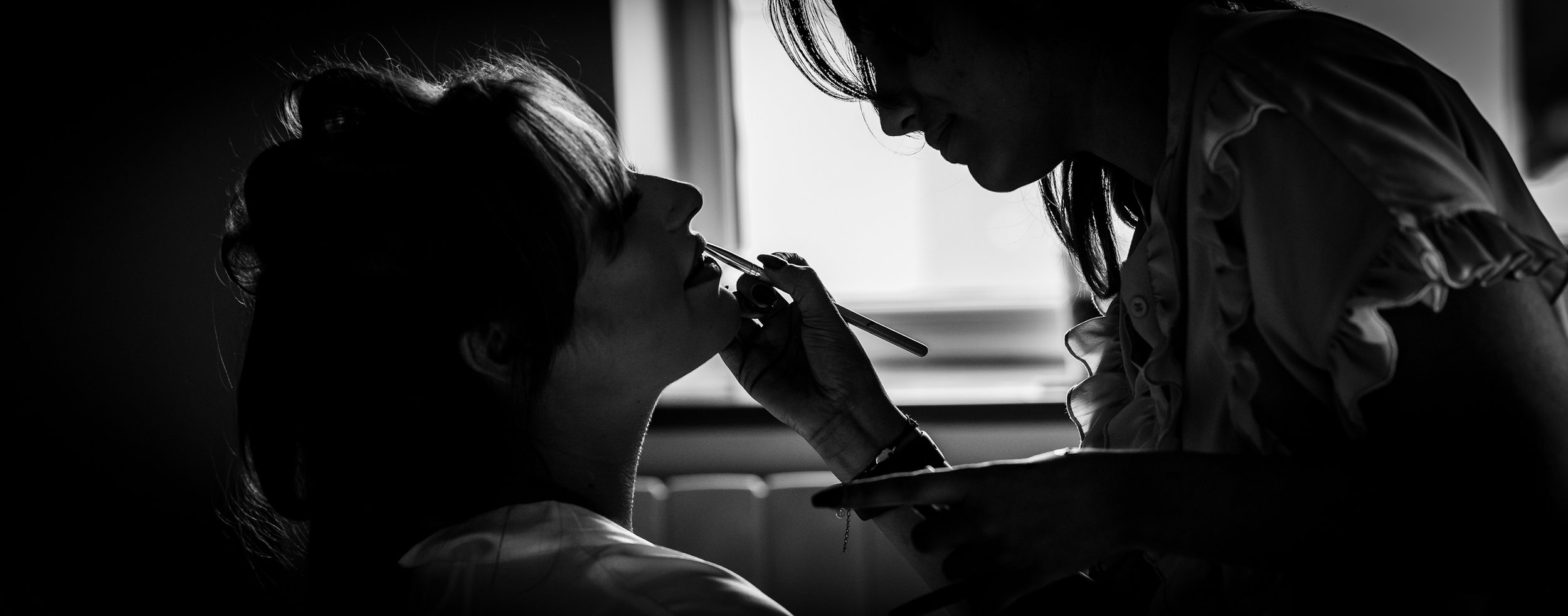 A black and white photo of one of the bridesmaids having her lipstick applied during bridal preparations