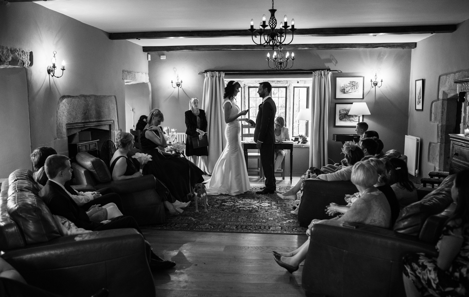 Black and white image from the back of the room while the bride and groom exchange their wedding vows