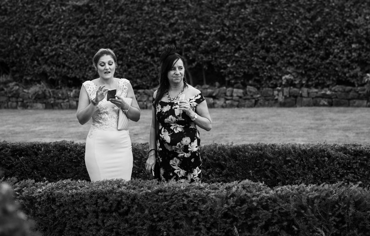 Black and white image of two of the wedding guests taking photos during the drinks reception