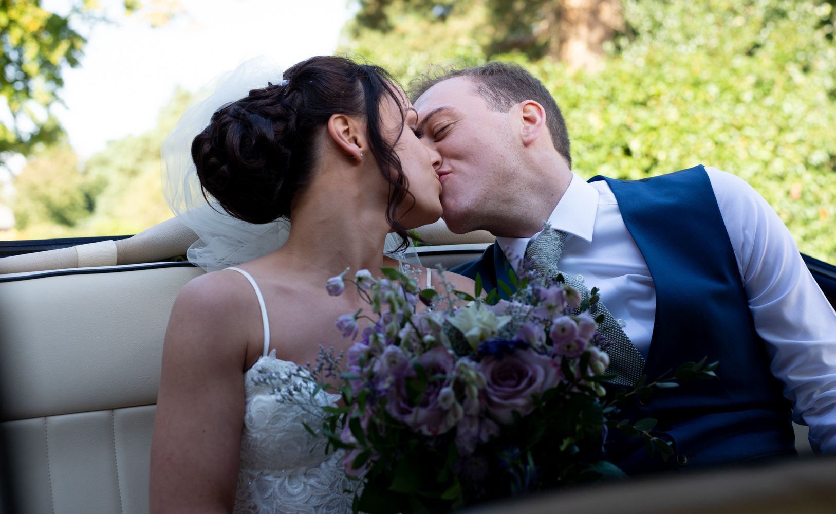 The bride and groom catch a sneaky kiss while sitting in the back of the car at the wedding reception