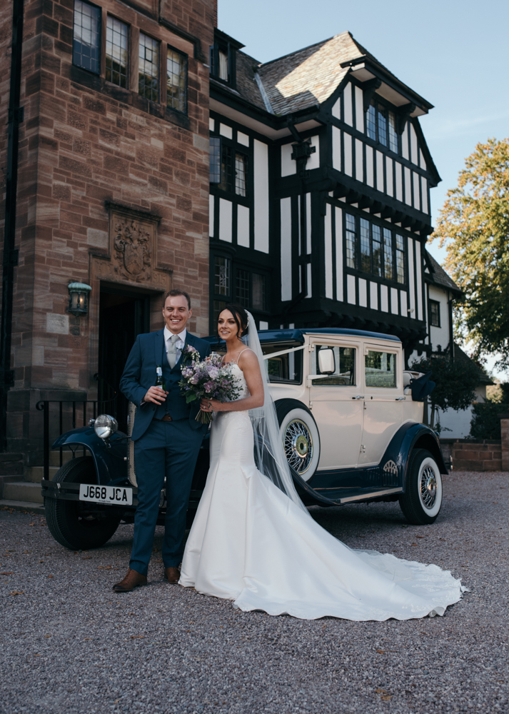 The bride and groom standing in front of the wedding car at Inglewood Manor