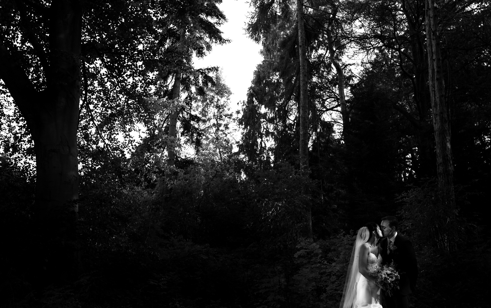 The bride and groom kissing in this black and white image in the woods