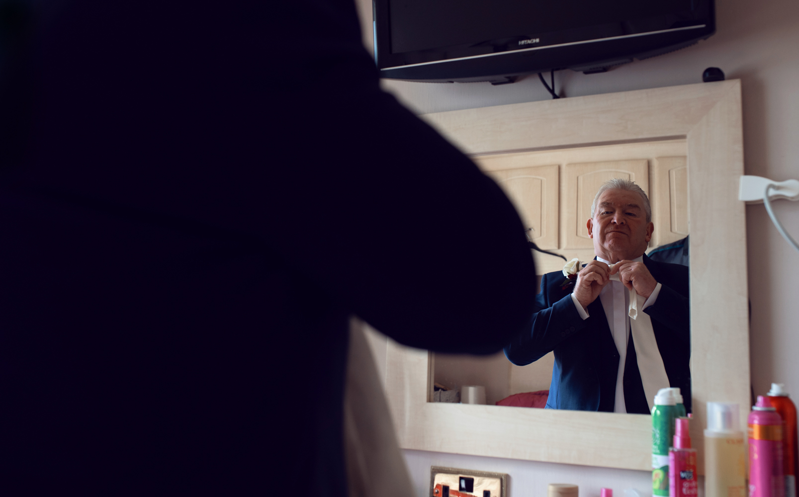 Image if the brides father adjusting his tie in the mirror