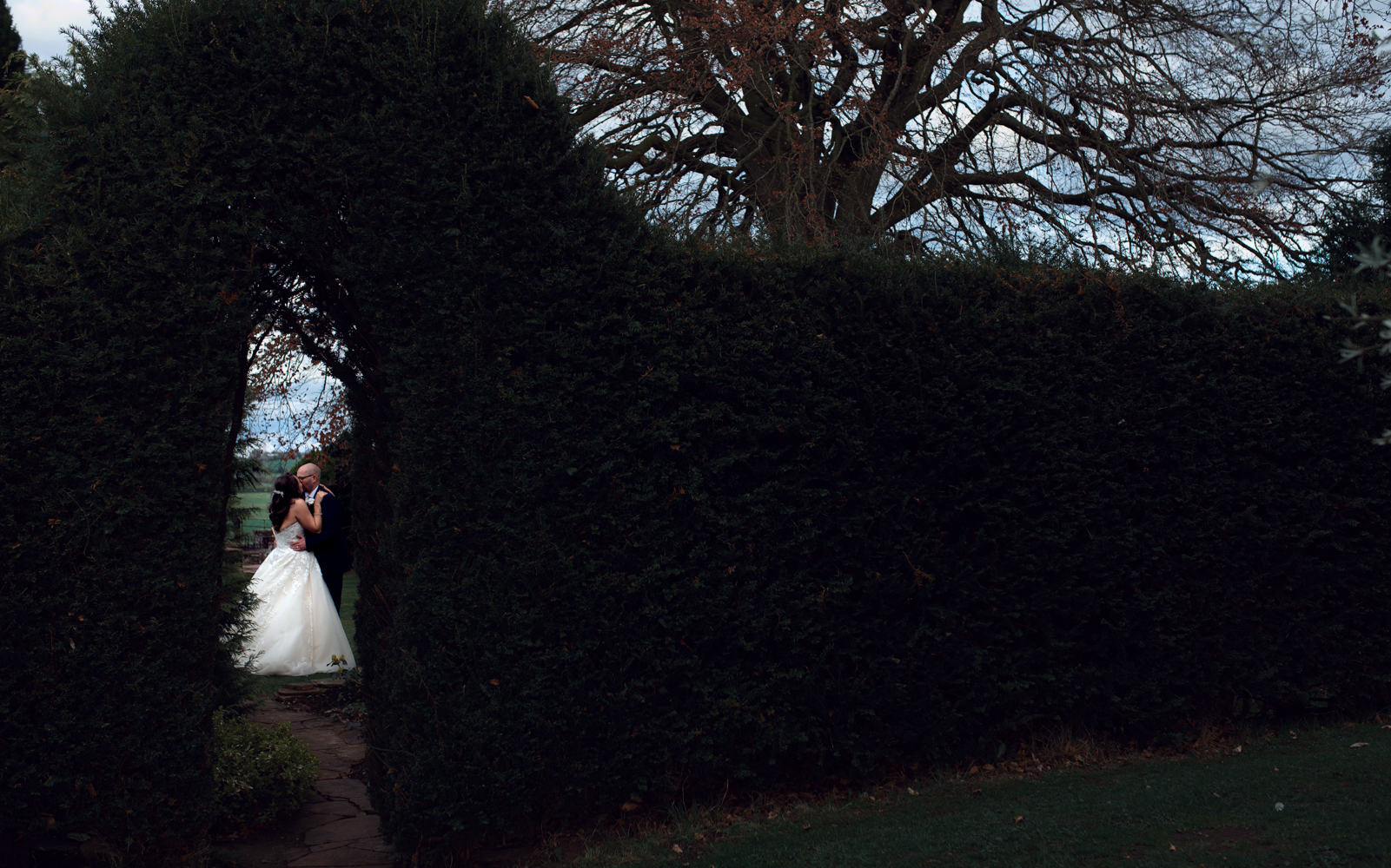The bride and groom through a gap in the hedge during couples portrait session