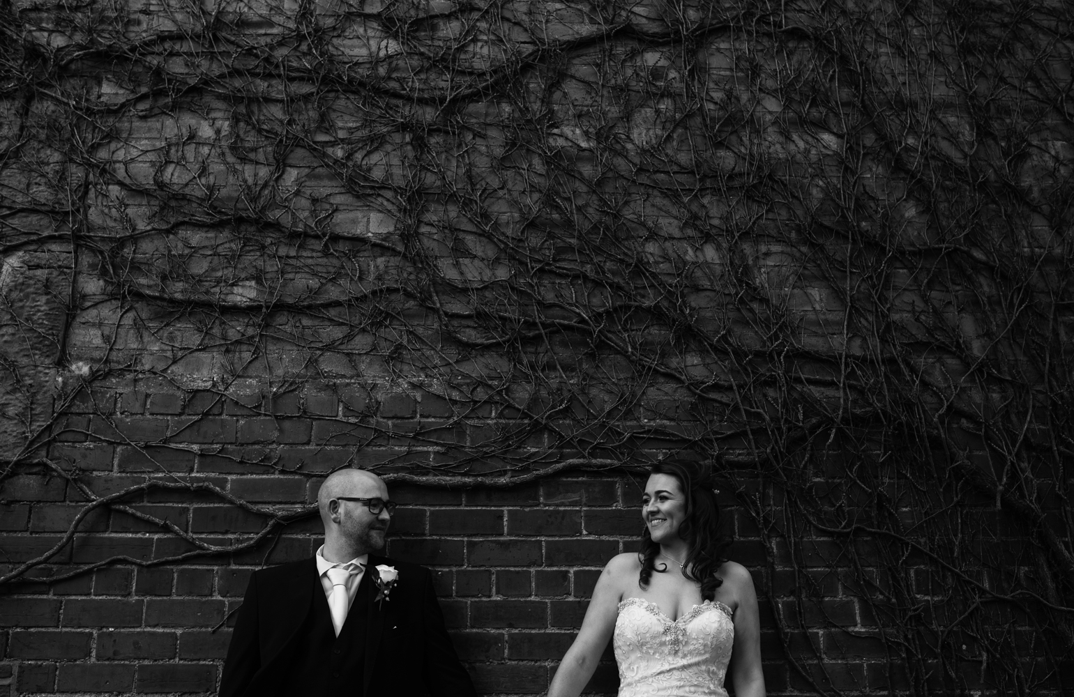 A black and white photo of the bride and groom standing in front of a wall during couples portraits