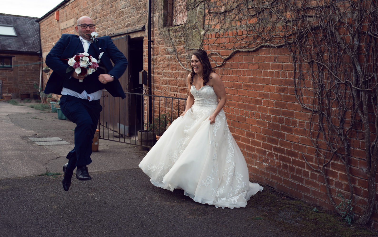 The bride laughing as the groom runs and jumps in front of her