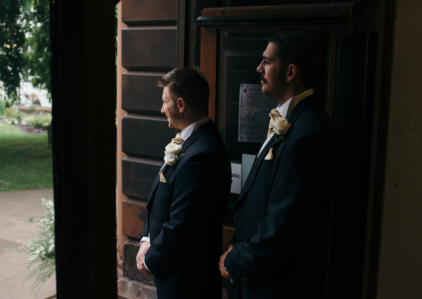 The groom and best man standing in the church doorway welcoming guests