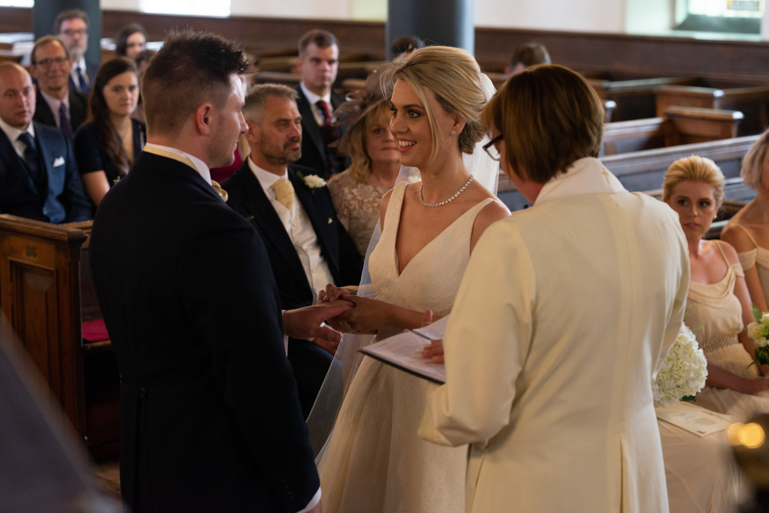 The bride and groom making vows before the vicar and congregation