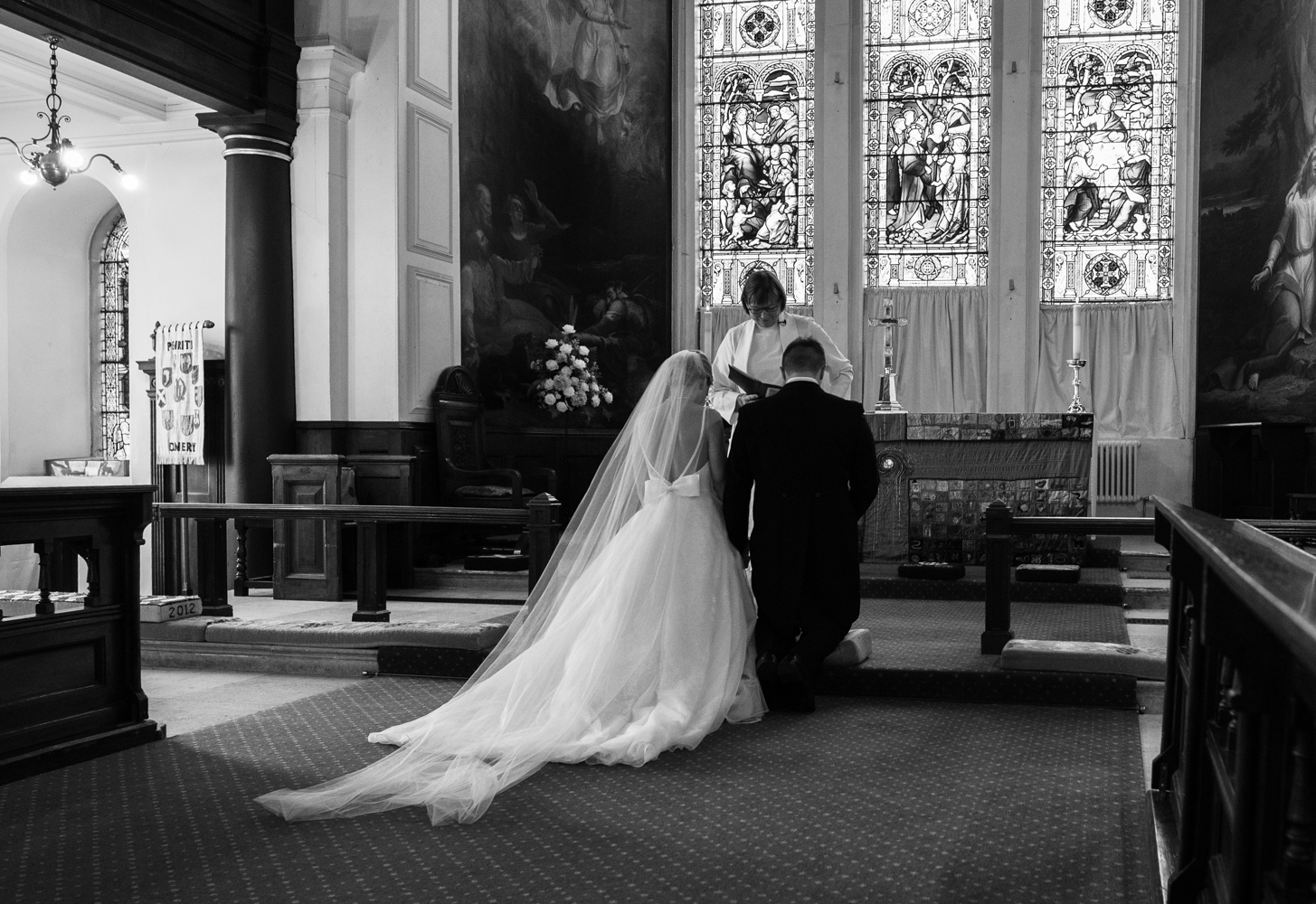A black and white photo of the bride and groom kneeling before the alter