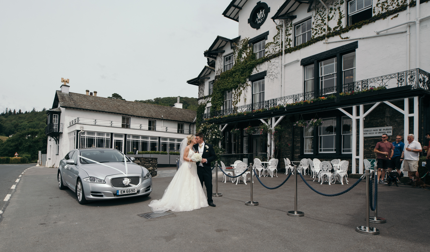 The bride and groom standing with the car outside of Low Wood Bay Hotel