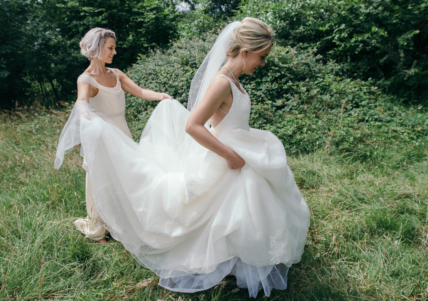 A bridesmaid helping the bride with her wedding dress during the couples portrait shoot