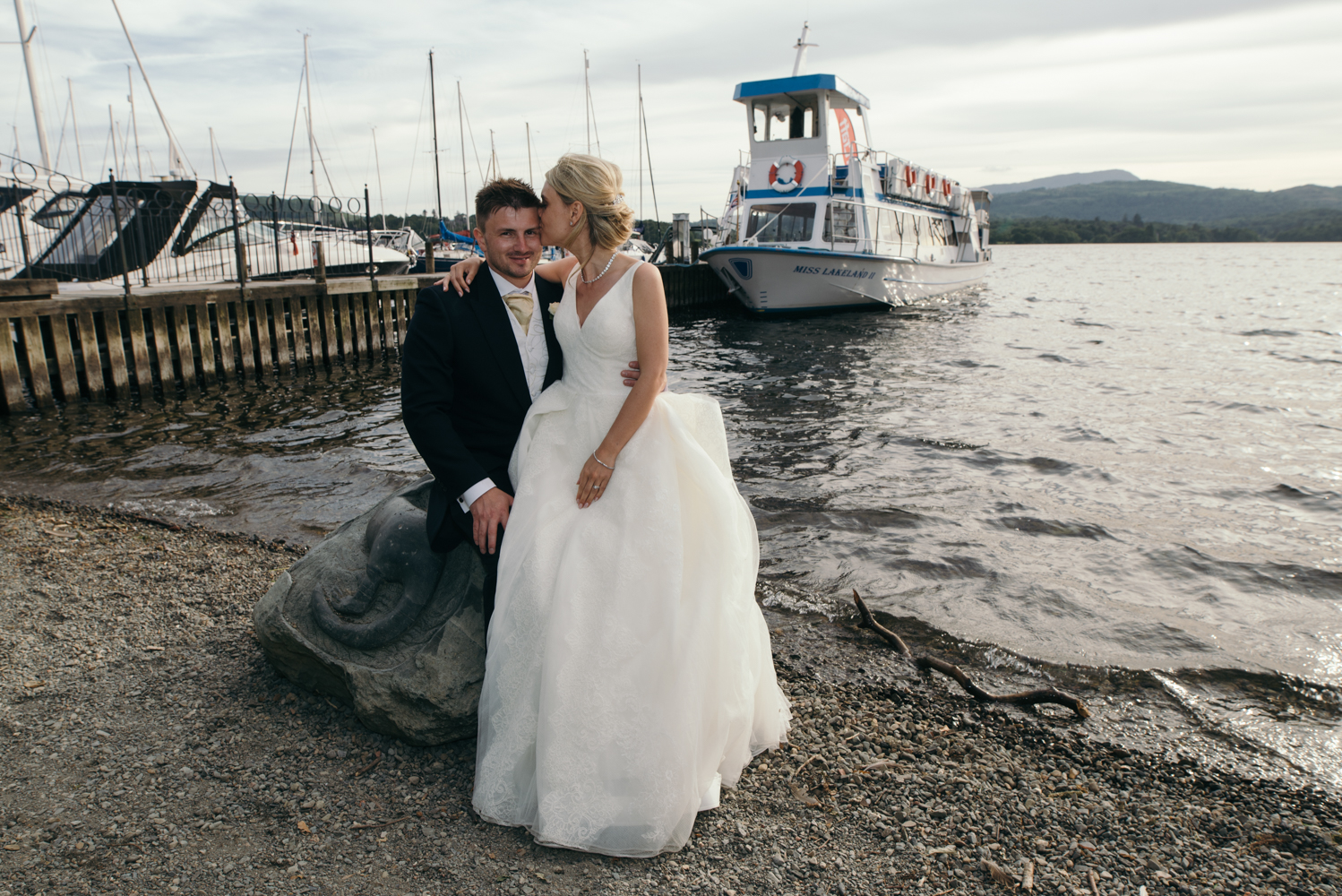 The bride and groom sitting on a commemorative stone by the jetty just after the lake cruise 