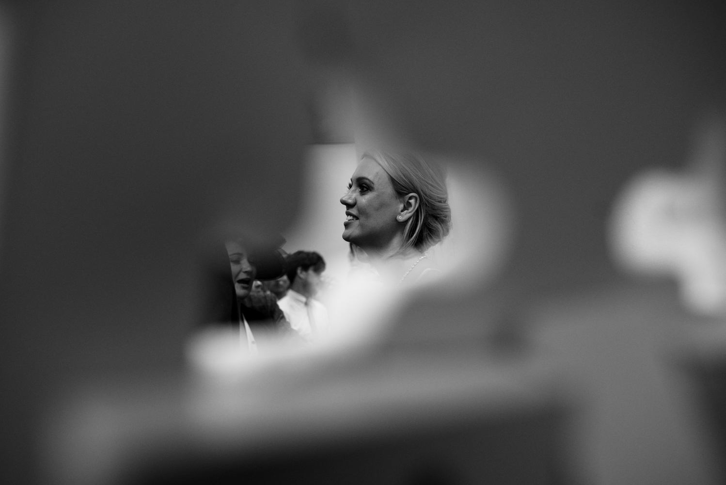 A black and white photo of the bride taken though a gap during the line up