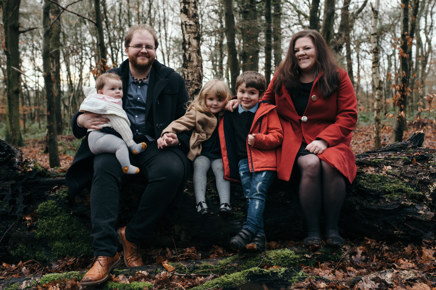 A family group photo sitting on an upturned log in the woods