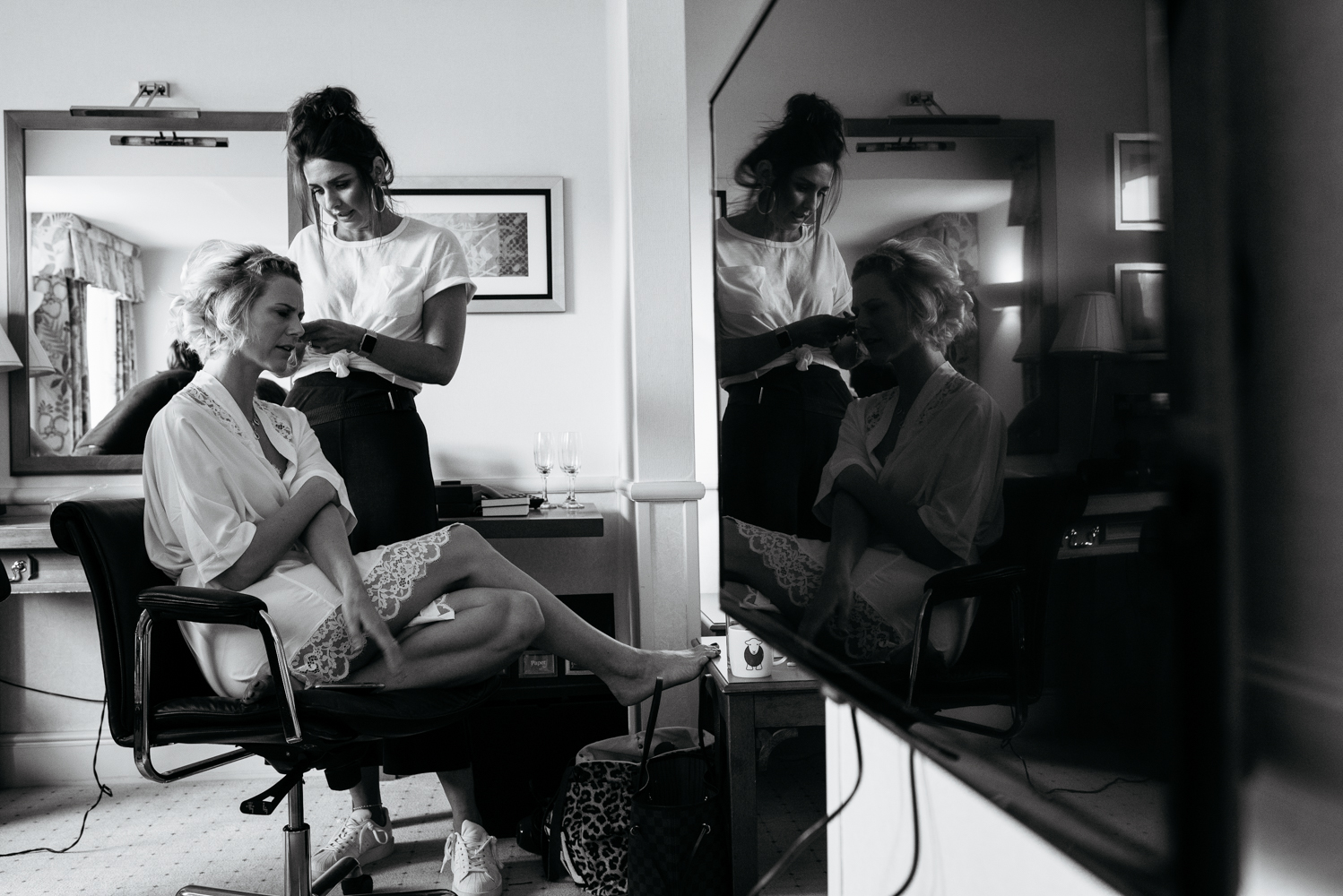 A black and white photograph of a bridesmaid having her hair done during morning bridal preparations