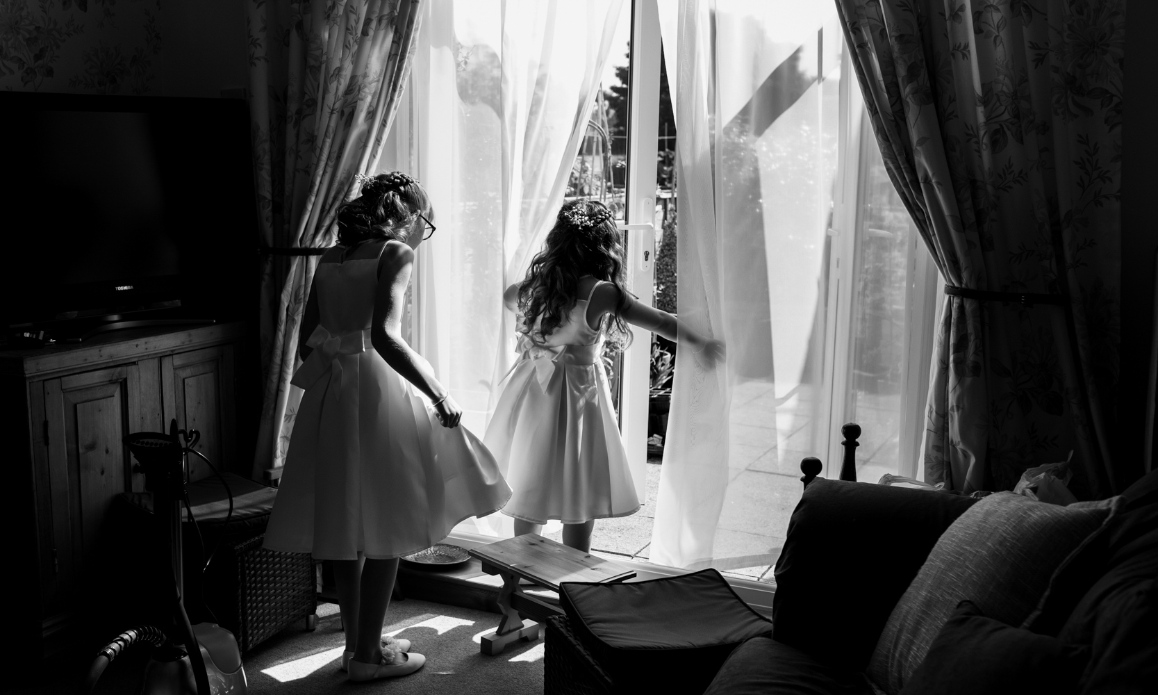 A black and white photograph of two young bridesmaids in their dresses playing about before leaving for the church