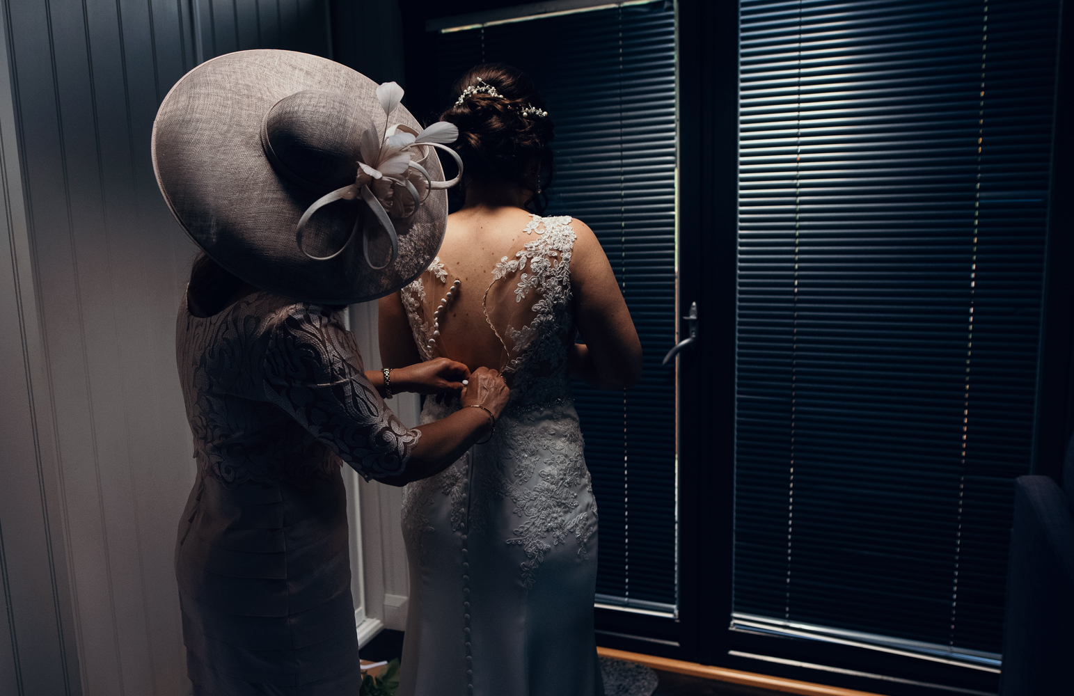 A bride being helped by her mum to fasten up the bridal gown before heading out to the ceremony