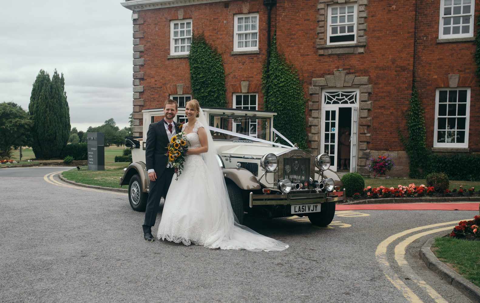 The bride and groom standing by the car at the entrance to the hotel