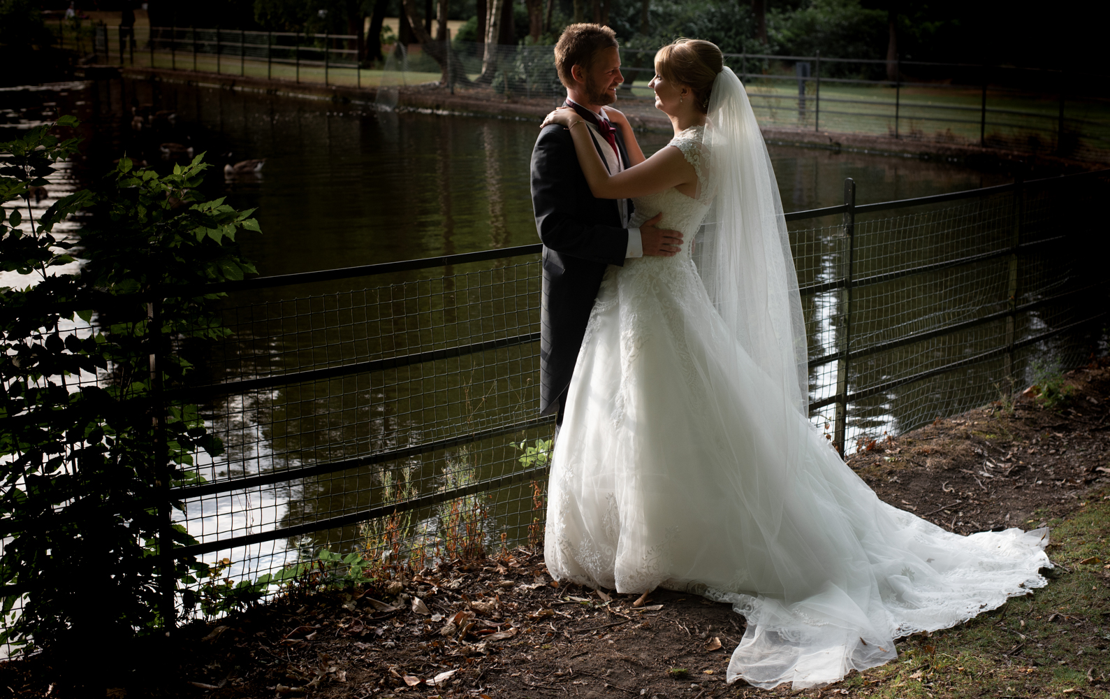 Another photo of the bride and groom standing by the lake in the early evening sunlight