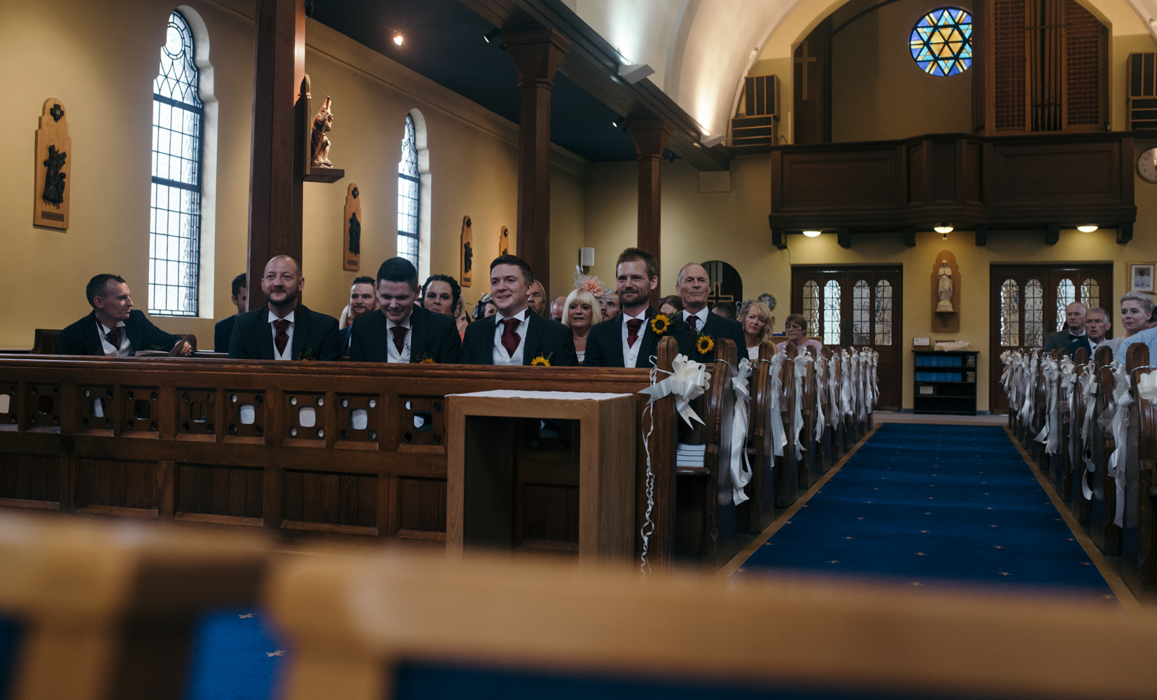 The groom best man and ushers sitting in the front rows of the church waiting for the bride and her father to arrive