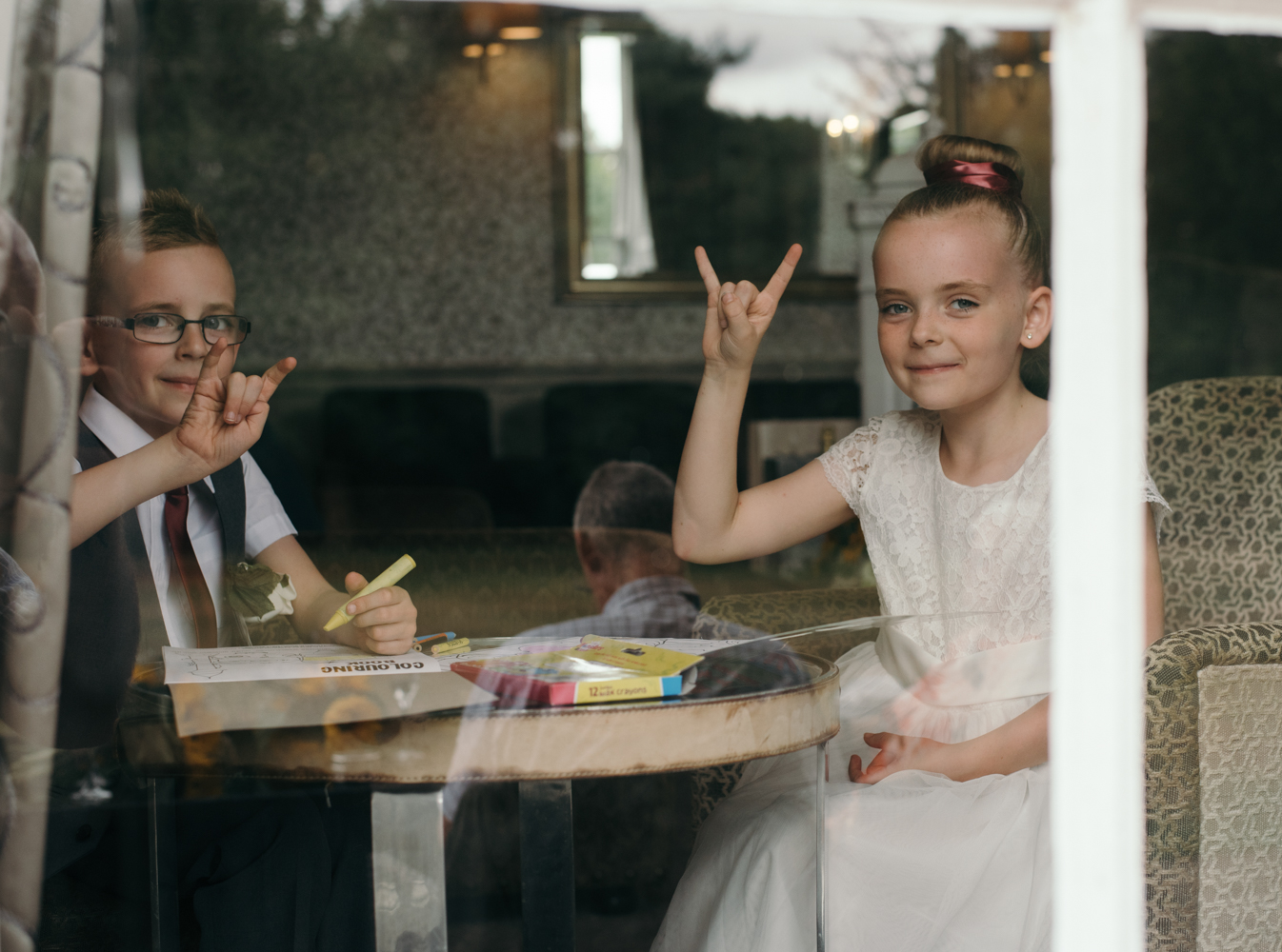 Tow young wedding guests doing the devils horns rock and roll sign through a window