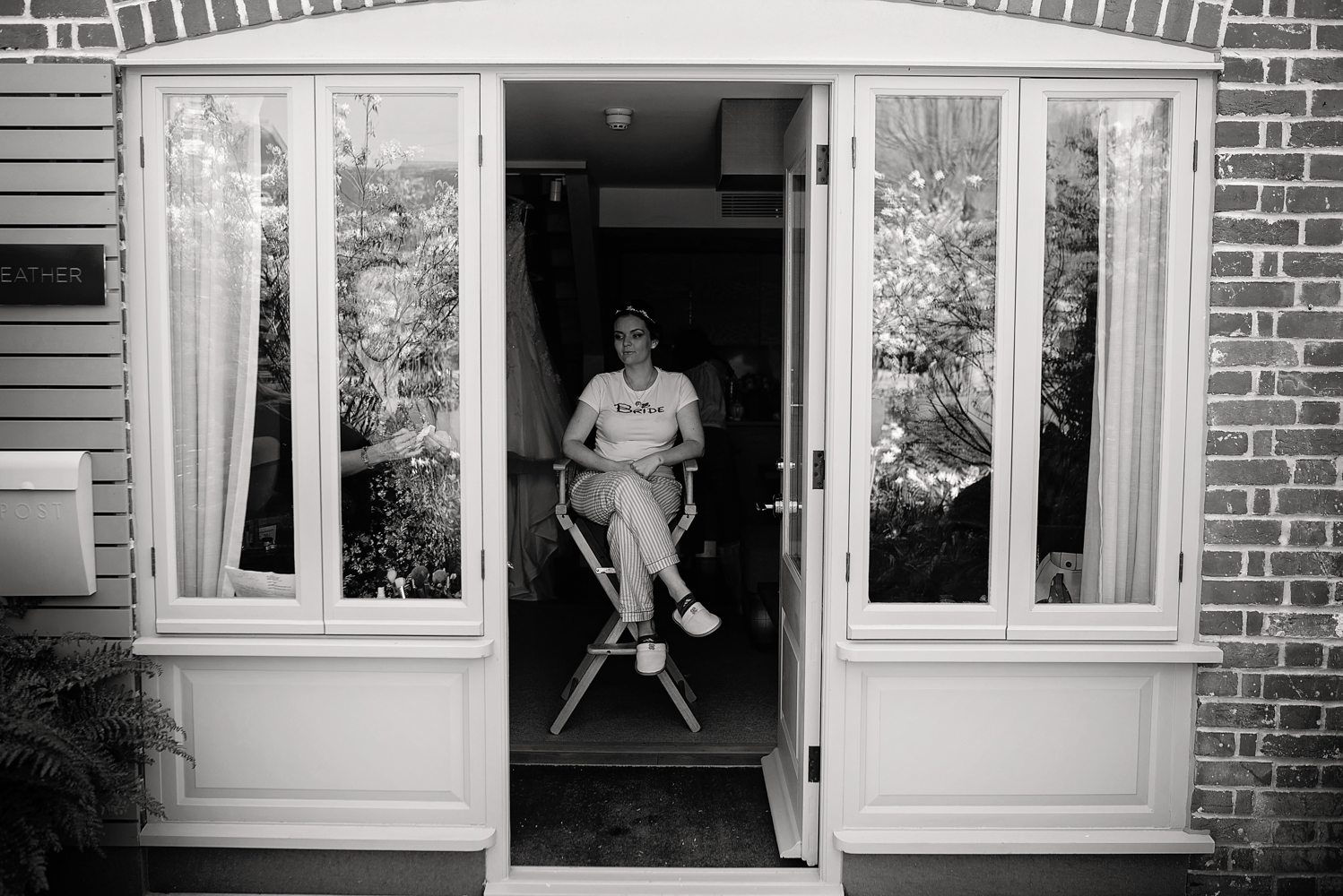 A black and white image of the bride sitting on a high chair having her makeup and hair done