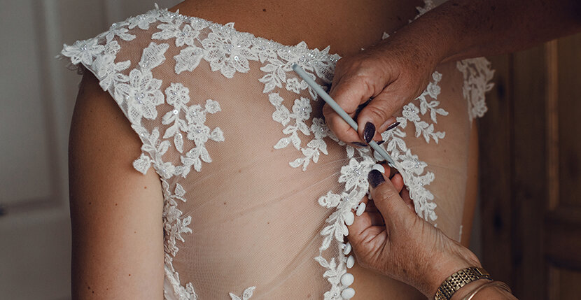 The bride having her dress buttoned up by her mum