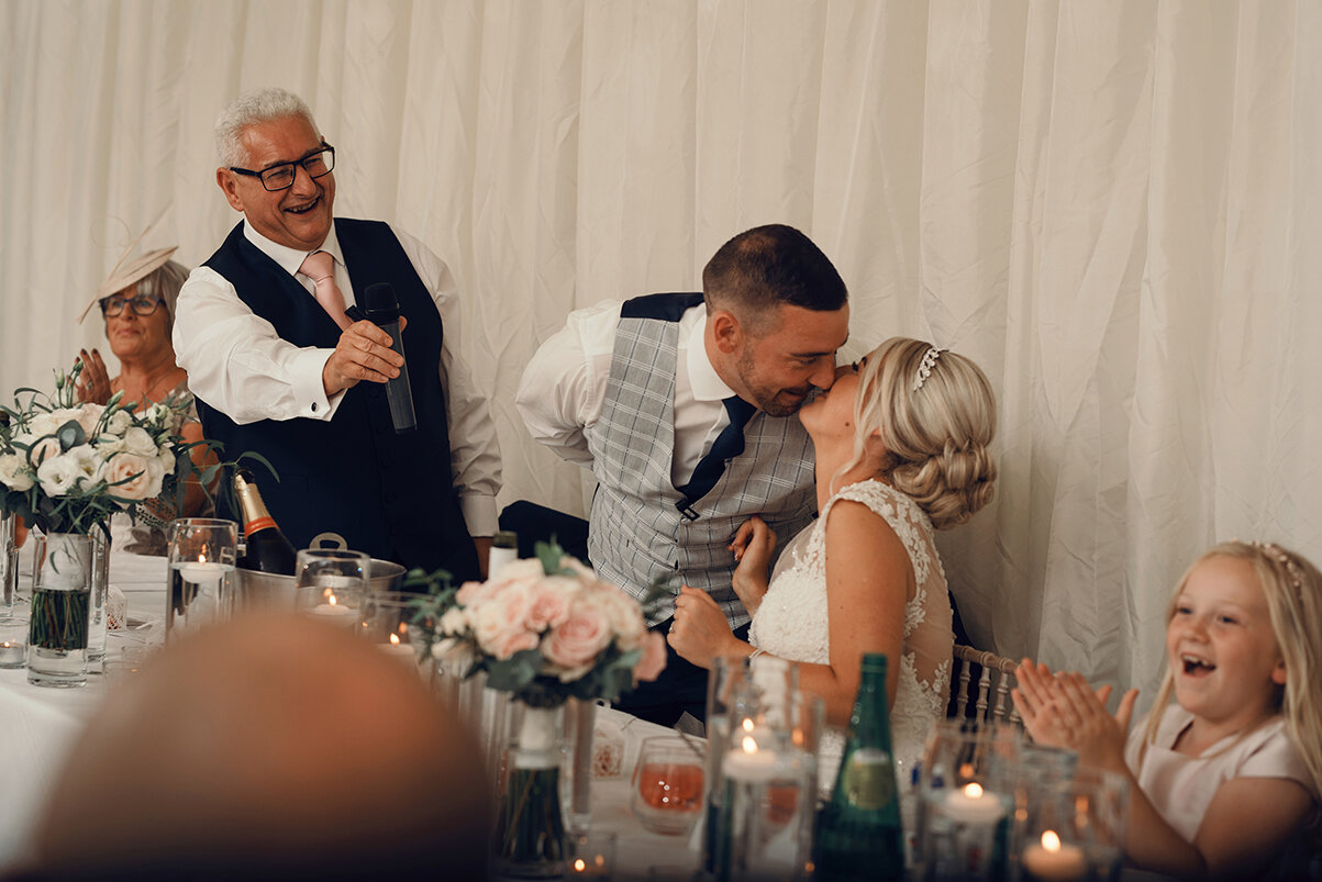 The groom gives the bride a kiss before he starts making his speech