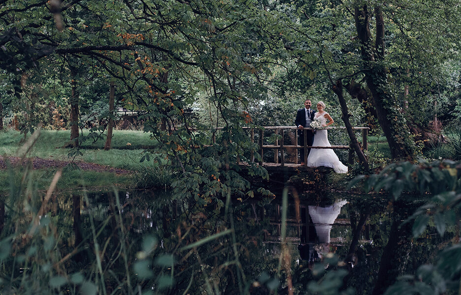 The bride and groom standing on a bridge in the woods