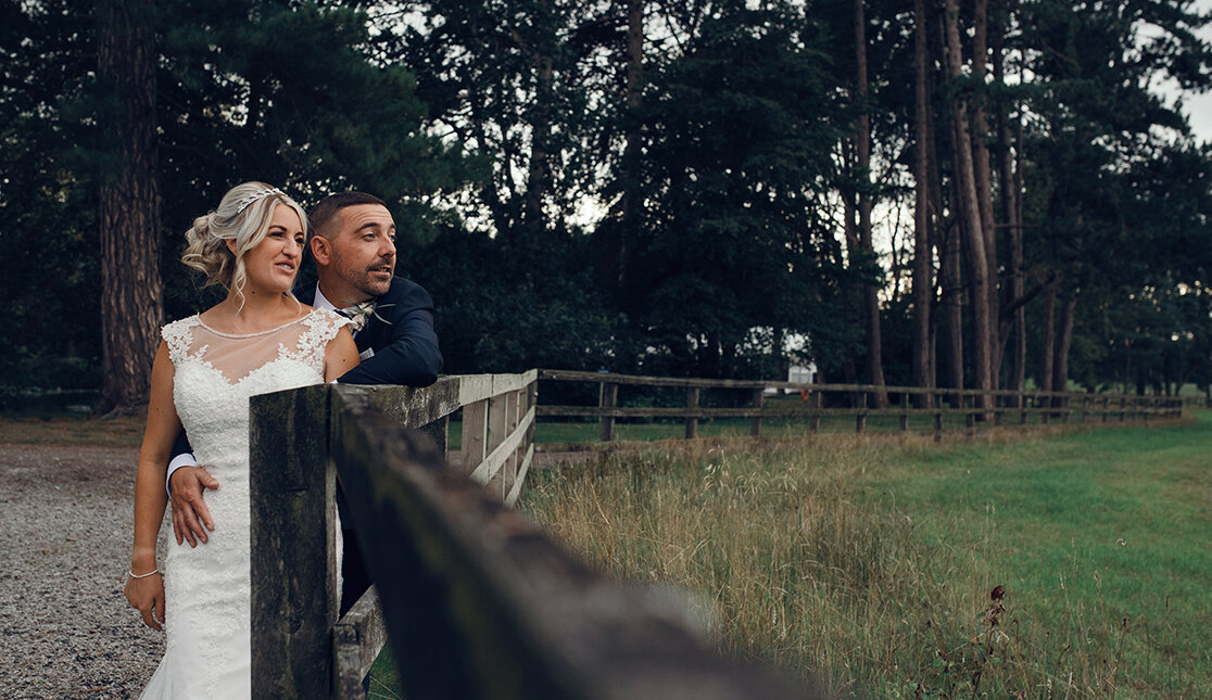 The bride and groom standing by a fence looking out across a field