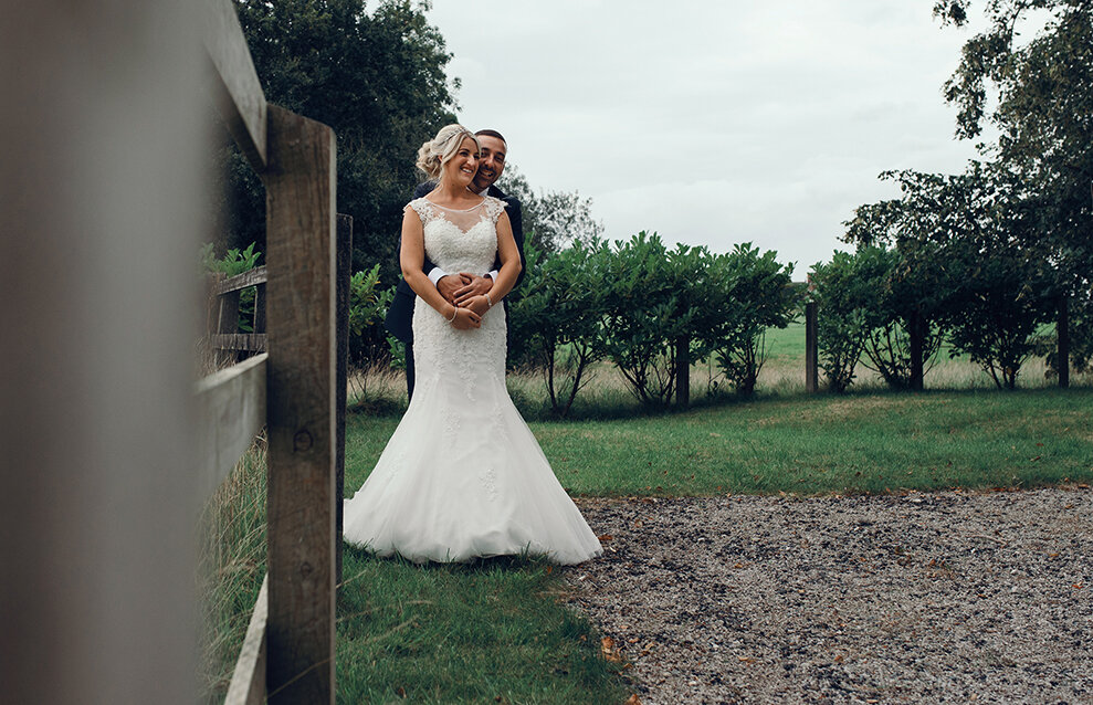 The bride and groom standing by a fence