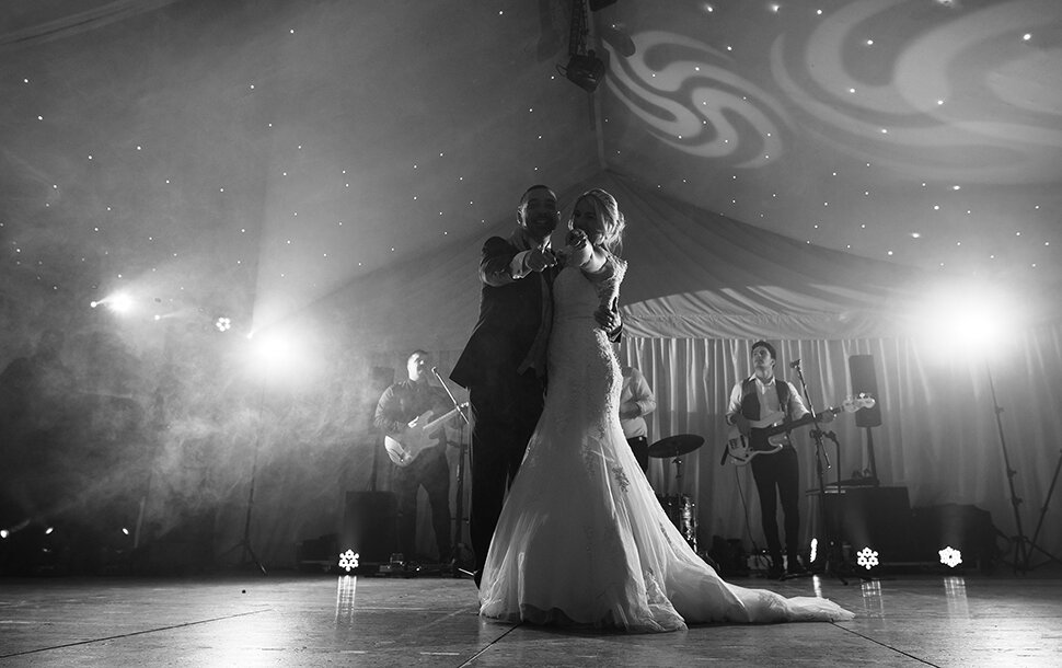 A black and white photo of the bride and groom both pointing towards the camera during the first dance