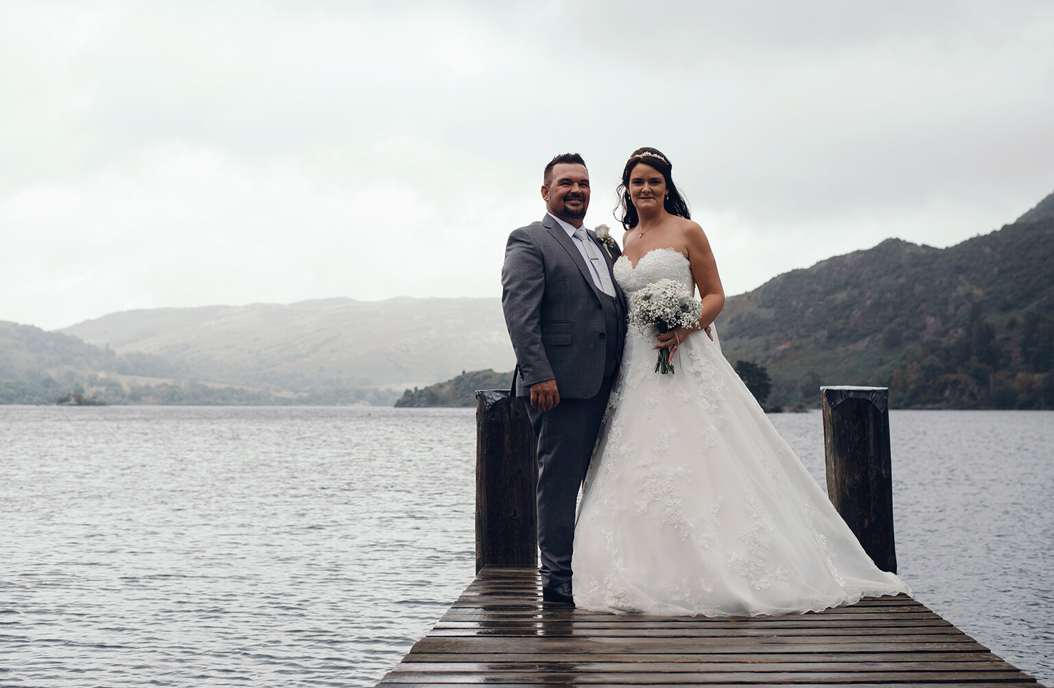 The bride and groom standing at the end of the jetty overlooking Ullswater