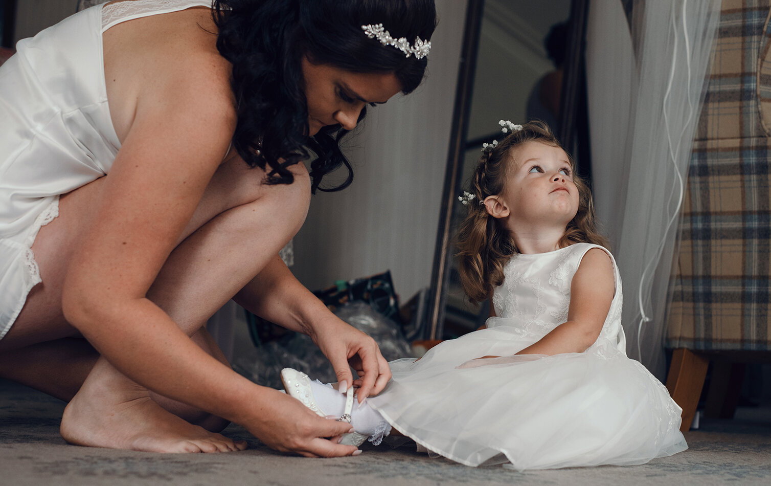 The youngest flower girl having her shoes put on by her mum the bride