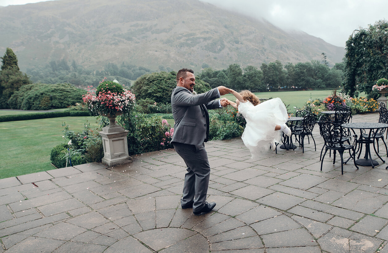 The groom twirling a flower girl around on the hotel patio