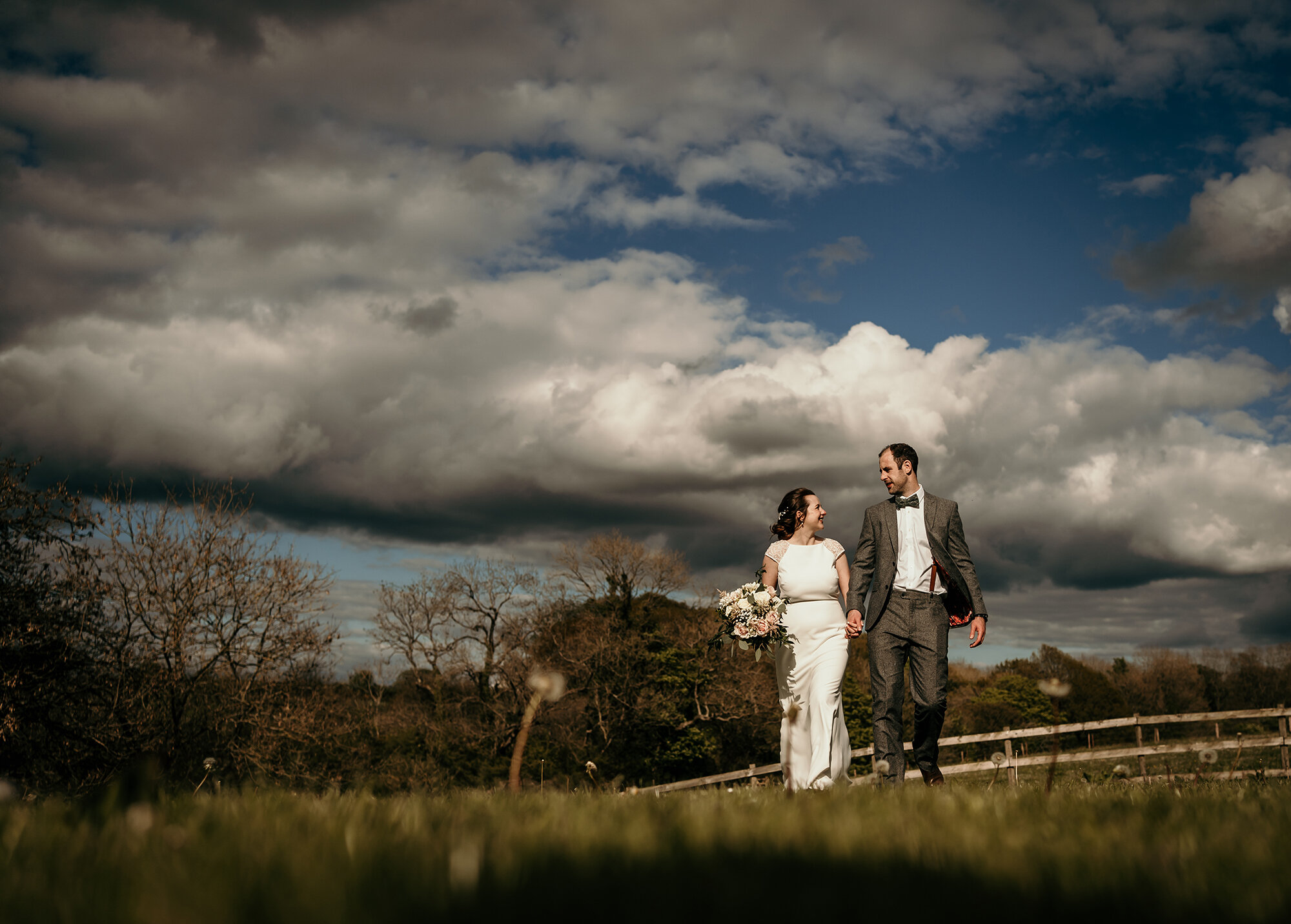 Bride and Groom walking through a field on their wedding day - Three Hills Barn