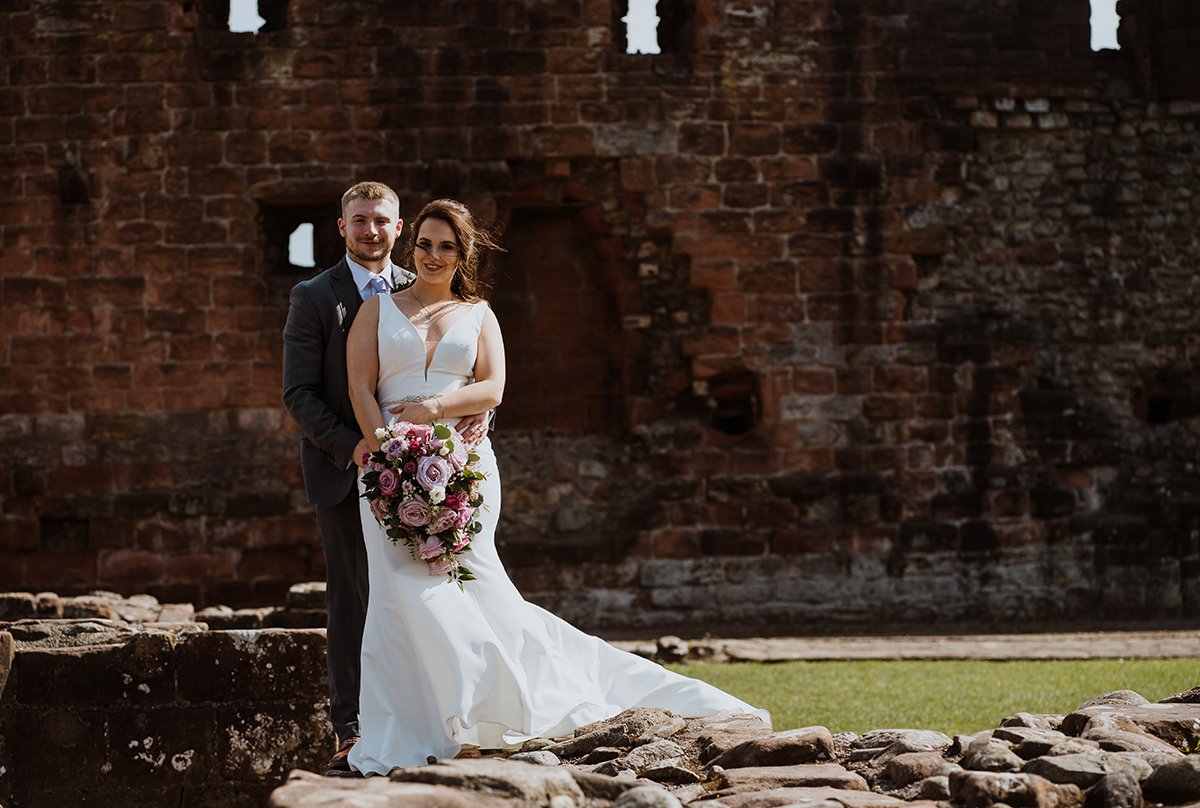 The bride and groom standing in front of the castle ruins