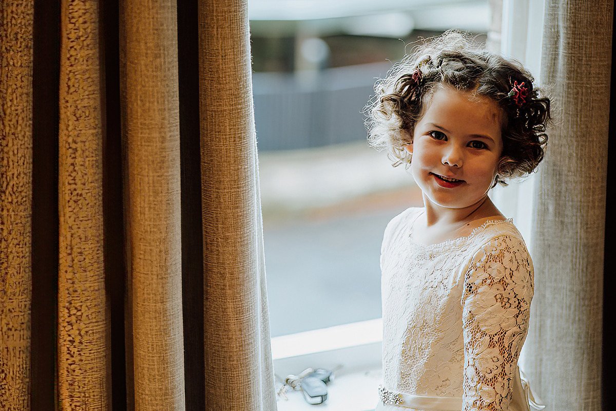 The flower girl standing by a window during morning bridal preparations
