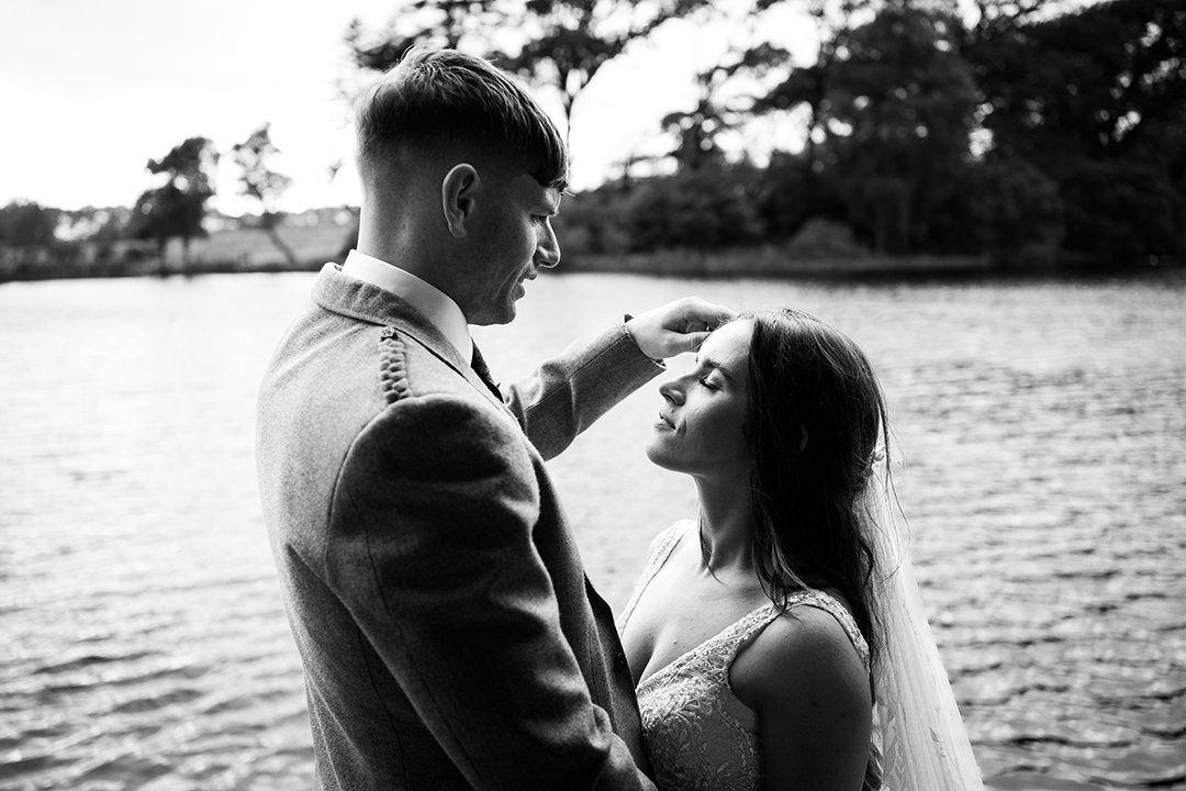 Black and white image of a groom touching his wifes hair during a portrait shoot