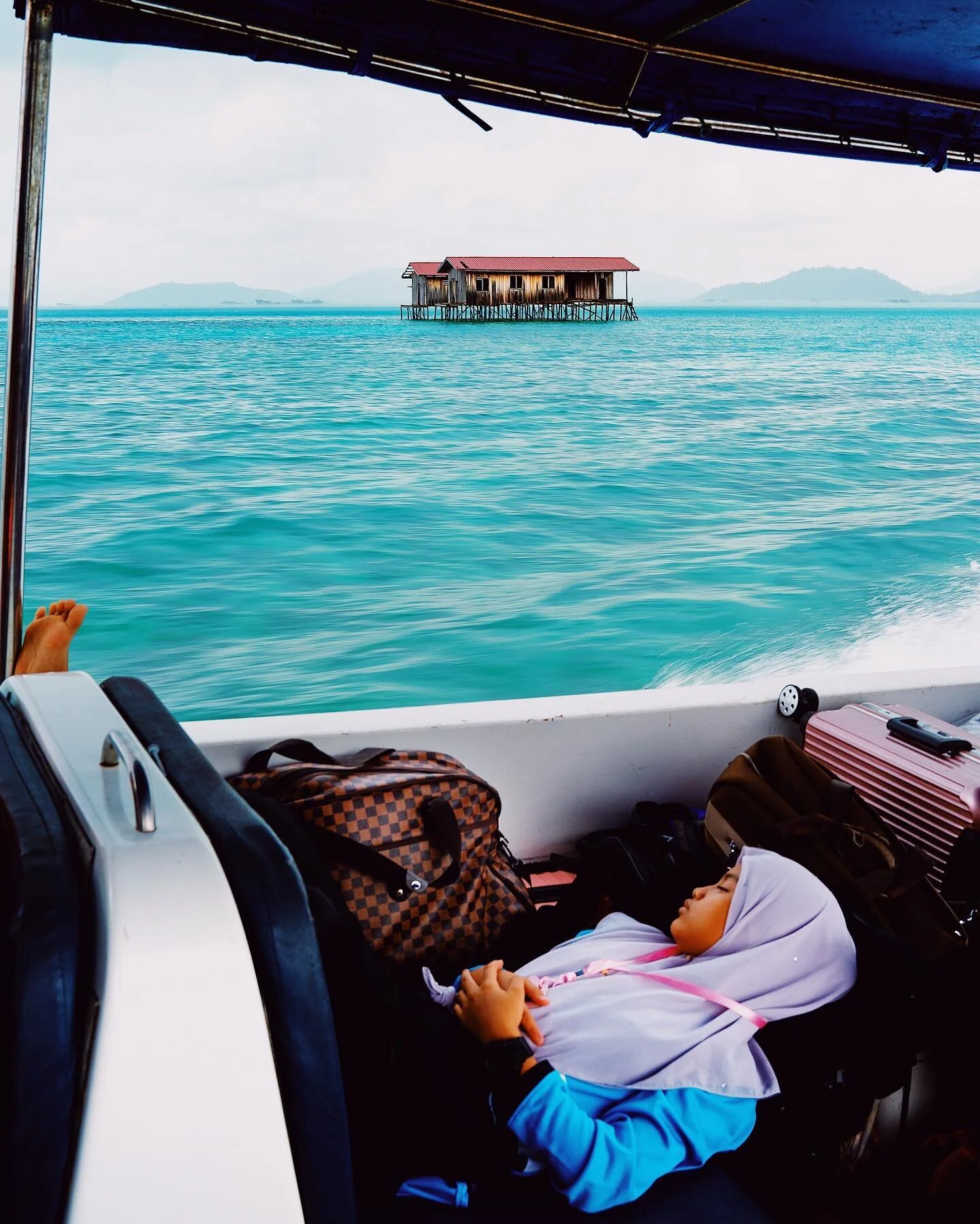 A Malay schoolgirl sleeping on luxury luggage on the way to Pulau Mabul. Mabul is a small, idyllic island sharply divided into two opposite halves. On one side, there are fancy dive resorts. Swaying coconut trees, crystal clear waters and incredible 